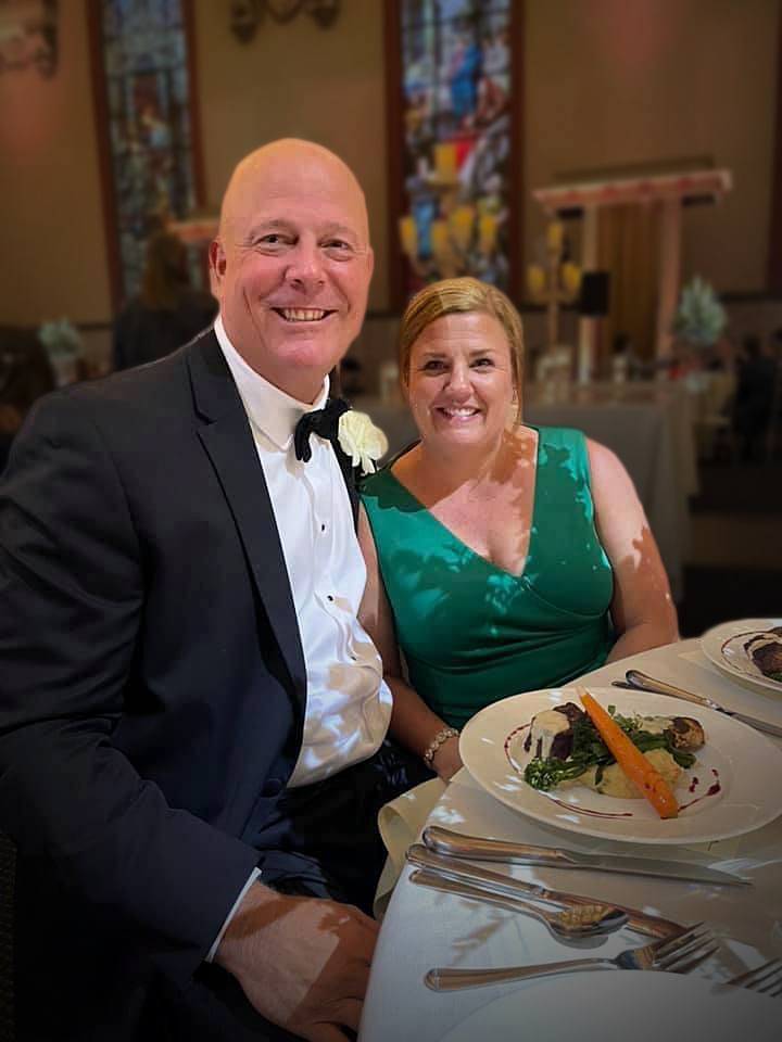 Couple smiling at formal event, elegantly dressed, enjoying a meal.